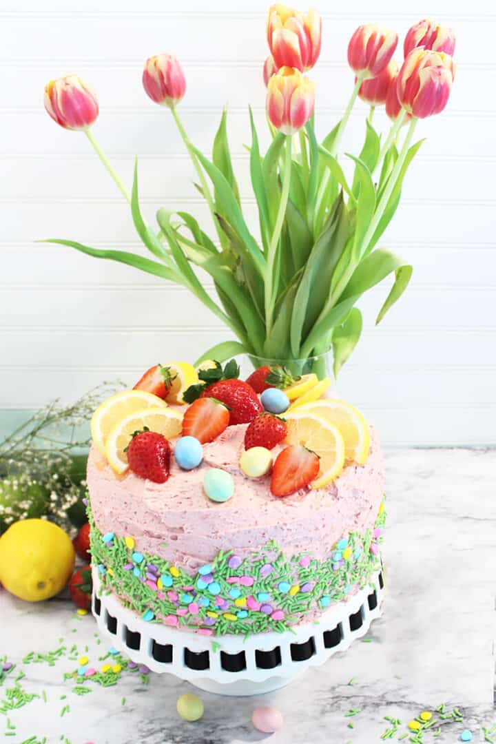 Decorated cake with sprinkle on side in front of tulips.