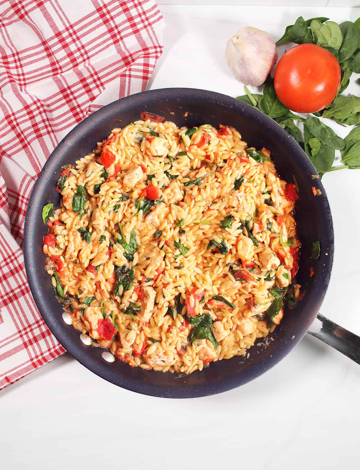 Overhead of chicken and orzo skillet in pan with checkered towel.