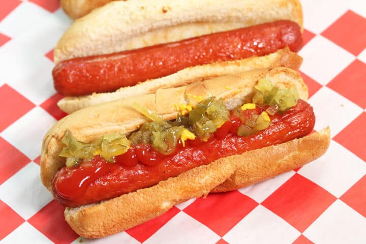 Closeup of dressed hot dog on red checkered paper.