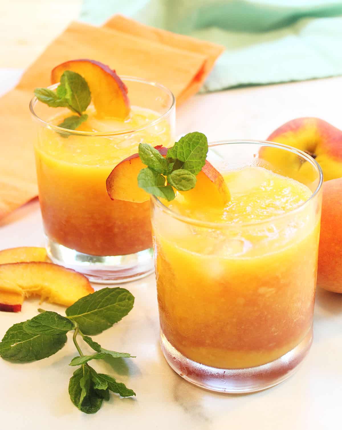 Two garnished Georgia Peach Cocktails on white table with peach napkin.