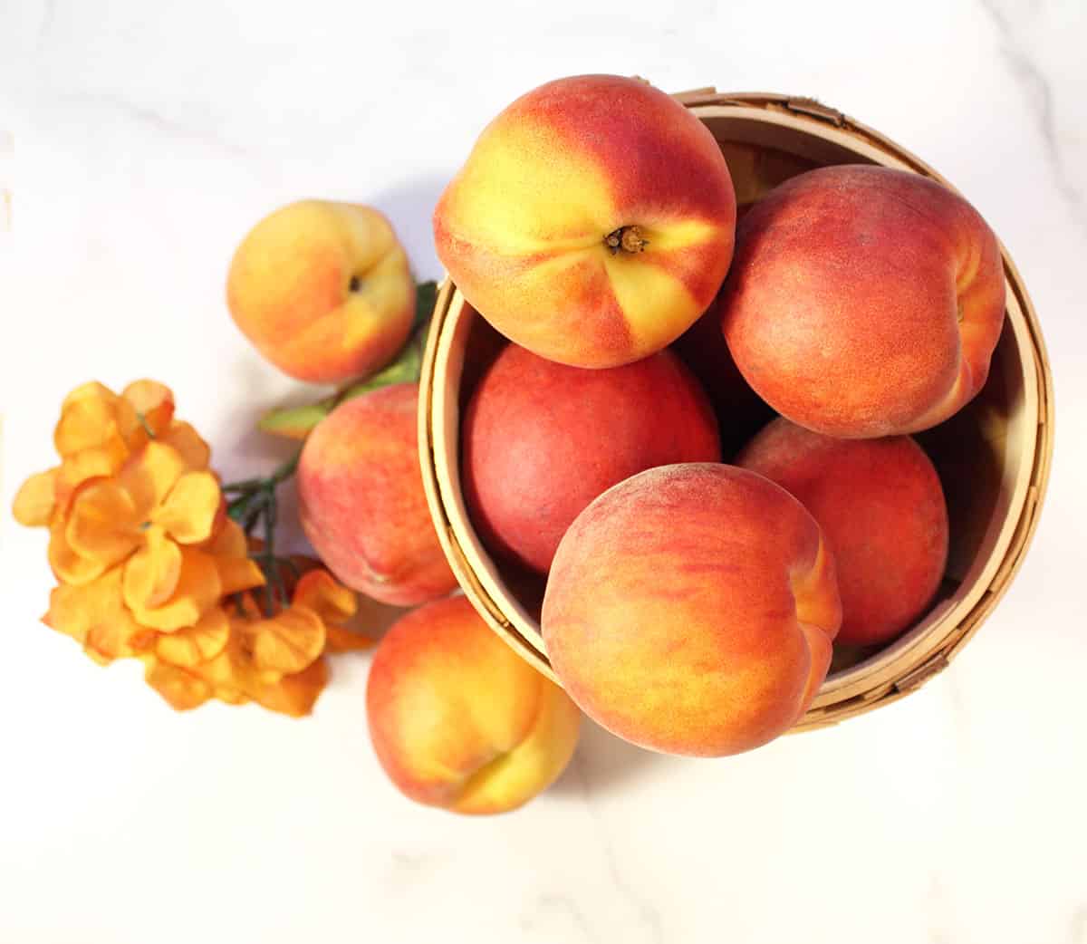 Peaches in a basket on white marble table.