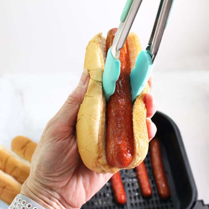 Placing air fried hot dog in bun.