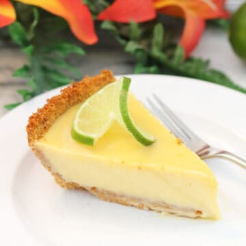 Slice of authentic key lime pie on white plate in front of flowers.