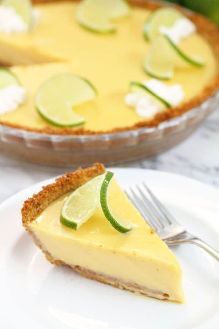 Slice of pie with fork on white plate in front of whole pie.