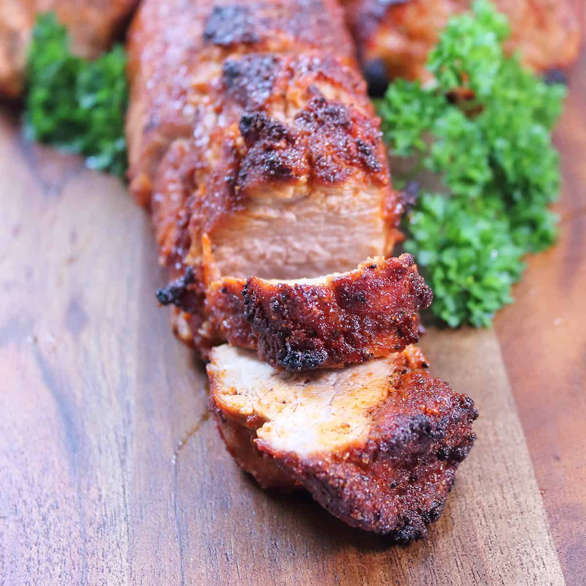 Closeup of sliced tenderloin on wooden serving board.