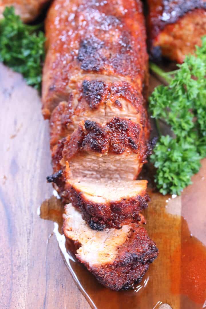 Closeup of sliced pork tenderloin on wooden serving board.