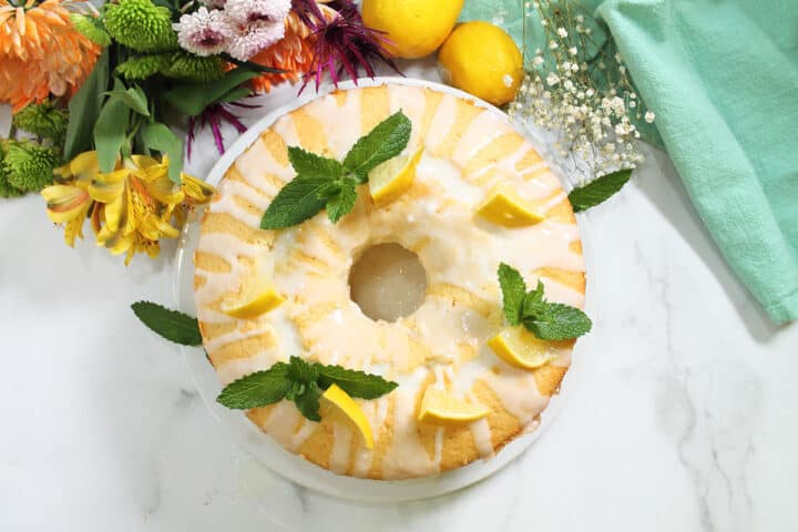 Overhead of decorated chiffon cake with lemon glaze, mint sprigs & lemon wedges.