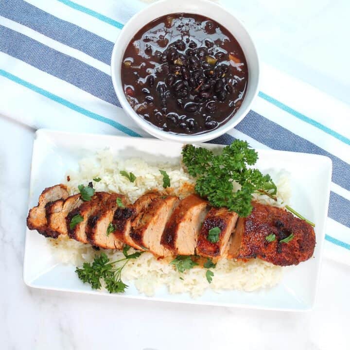 Overhead of pork on platter on top of rice with black beans on side.