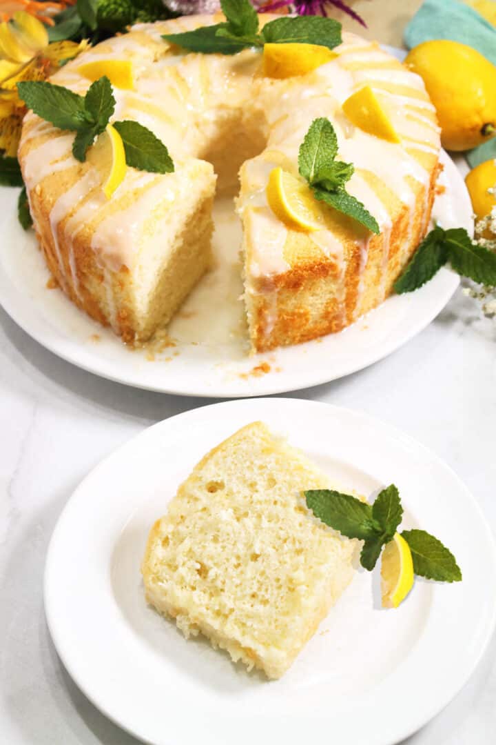 Slice of lemon chiffon cake on white plate with whole cake in background.