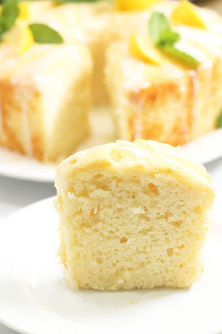 Closeup of slice of lemon cake with whole cake in background.