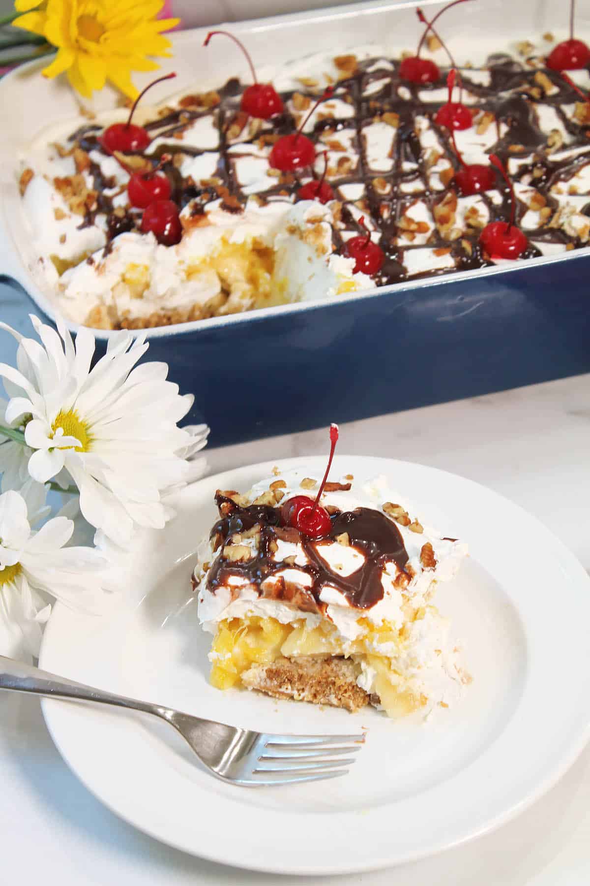 Slice of Banana Split Cake on plate with full cake in background.