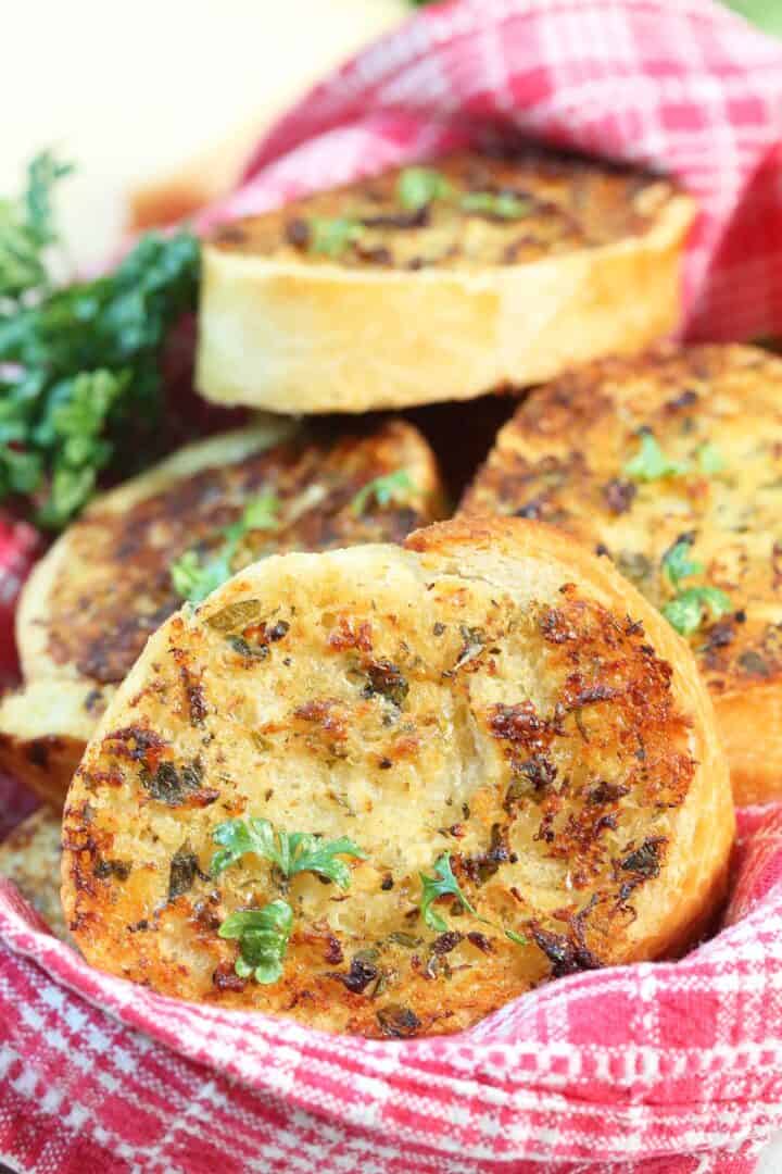 Closeup of garlic bread in basket lined with red checkered linen.