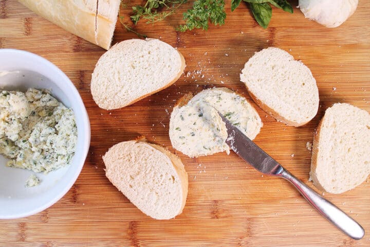Spreading butter onto slice of bread on wooden cutting board.