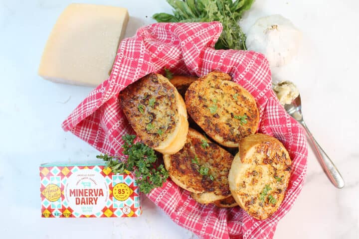Overhead of garnished bread in basket lined with red checked towel and Minerva butter package.