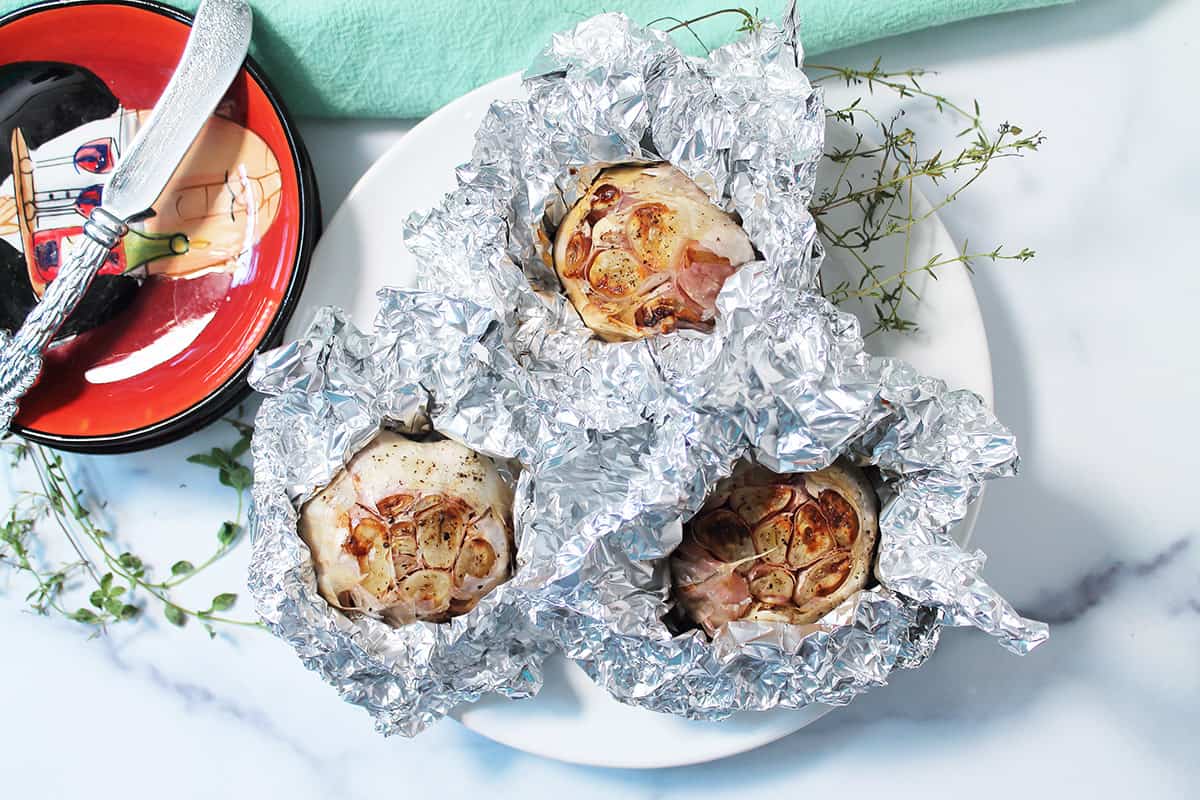 Three roasted garlic heads on white plate.