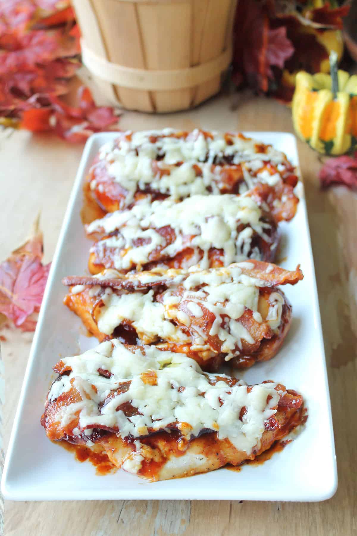 Baked BBQ chicken breasts on serving platter on wooden table.