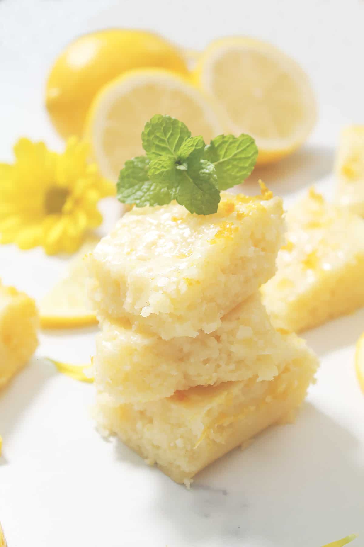 Stacked lemon brownies on white marble table with mint leaf on top.