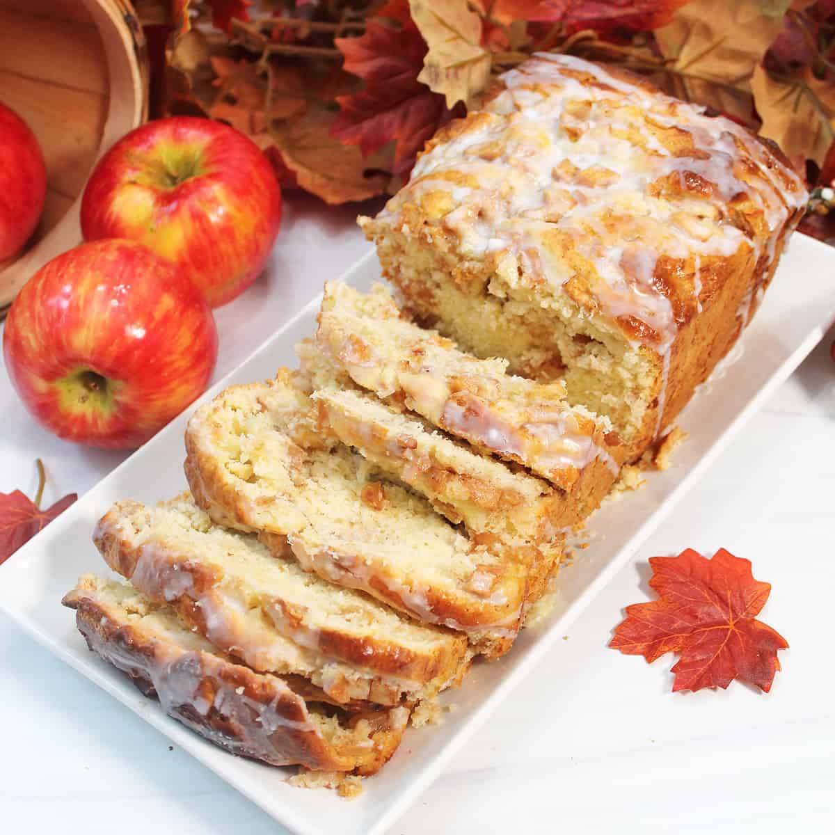 Sliced glazed apple cinnamon bread on white platter with apples.