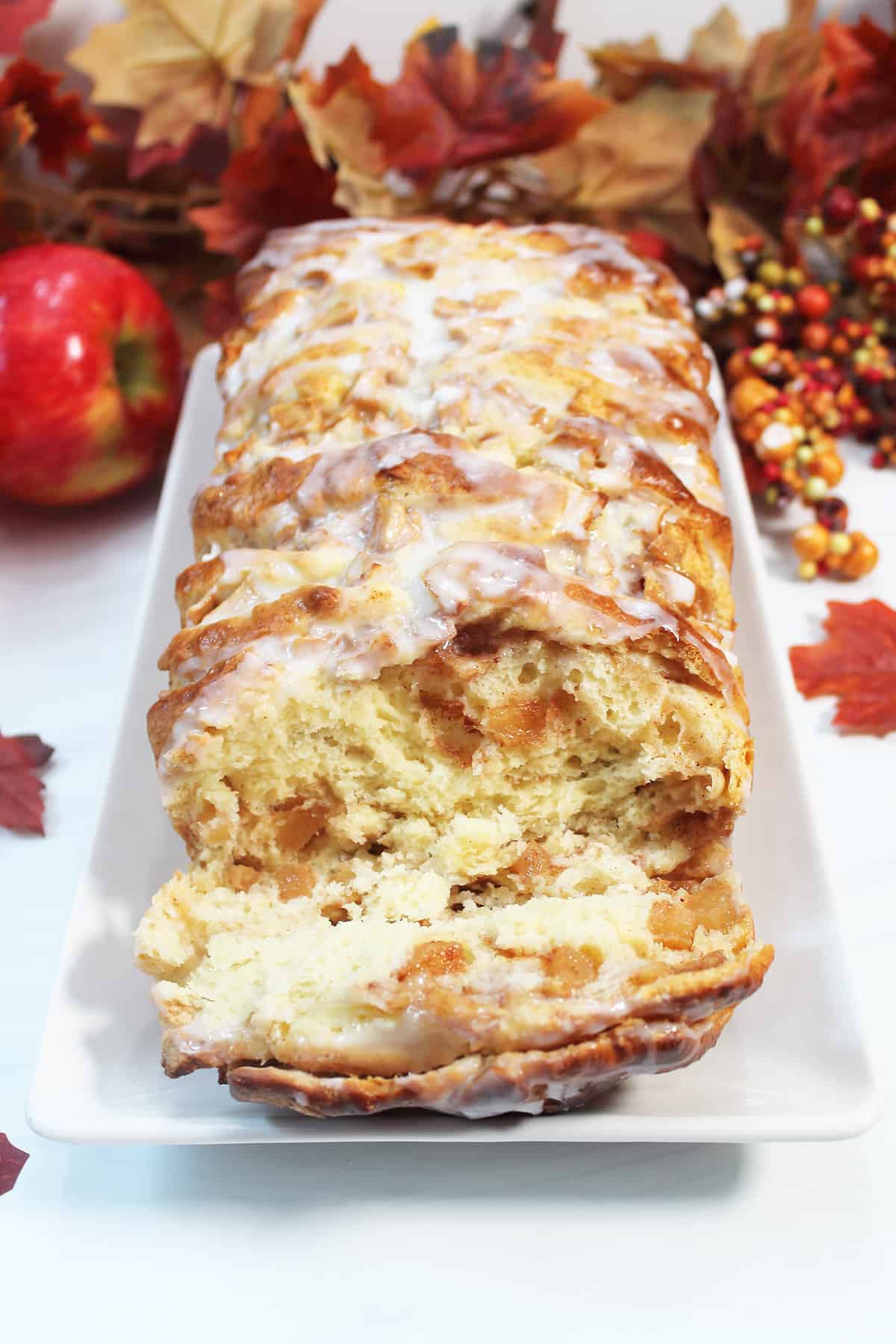Loaf of apple cinnamon bread on white platter with fall leaves in back.
