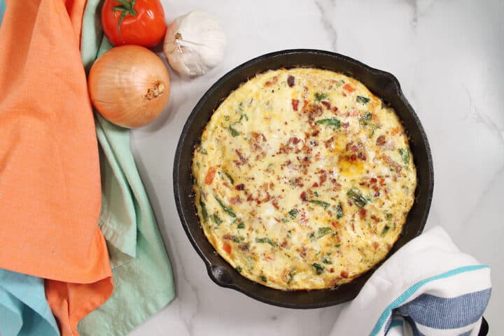 Baked frittata with towel around handle next to orange and green napkins.