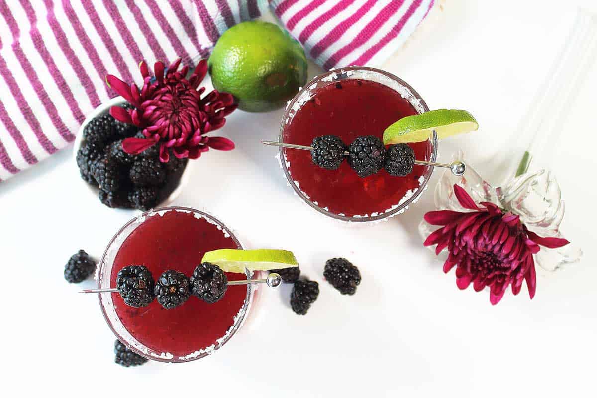 Overhead of two cocktails with bowl of blackberries.