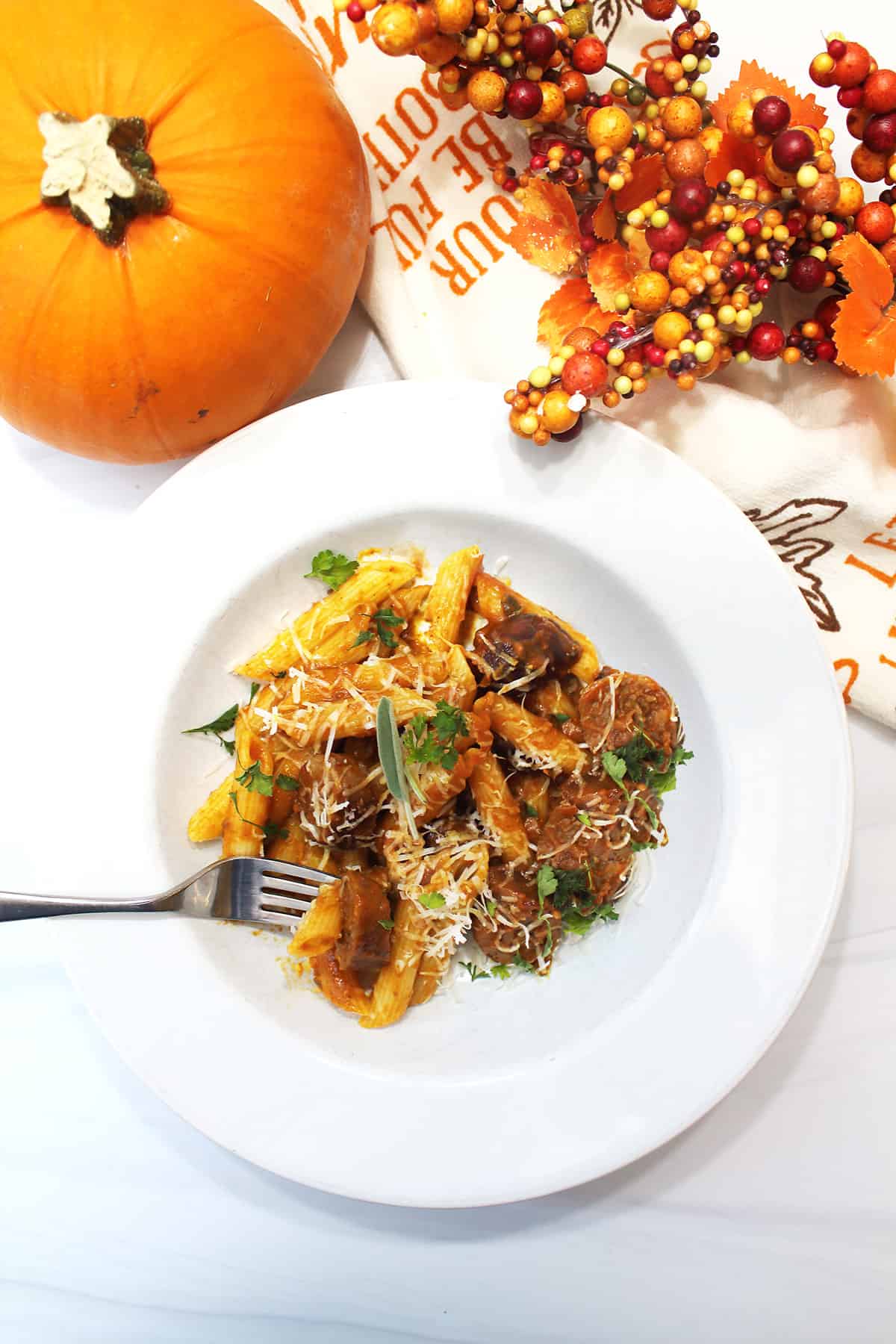 Overhead of pasta serving in white bowl with fork and pumpkin and berries in back.