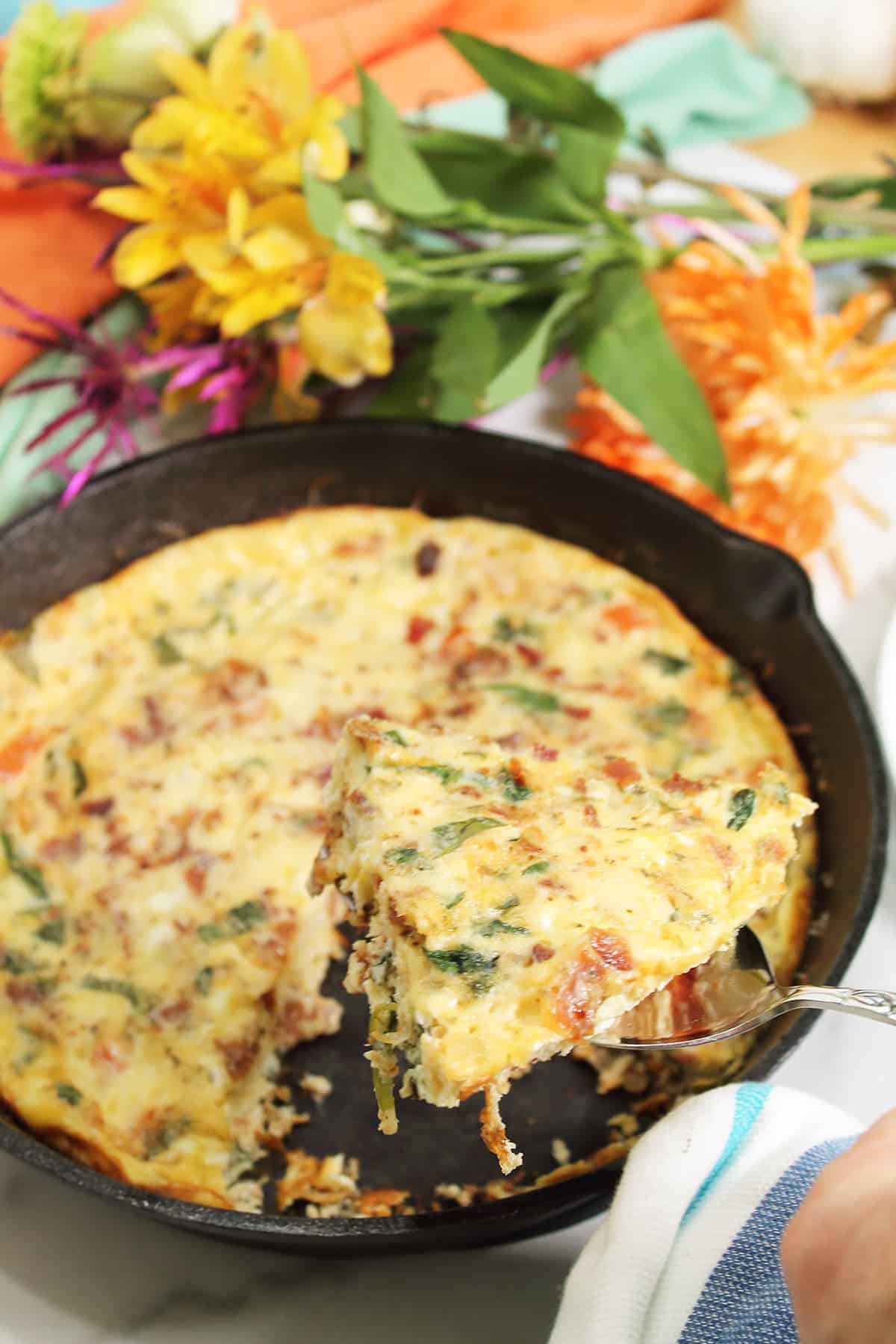 Lifting serving out of iron skillet with flowers in back.