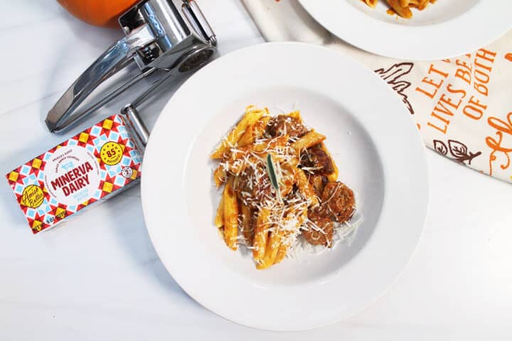 Overhead of bowl of pasta with sausage and cheese grate and Minerva butter package on side.