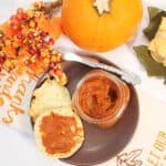 Overhead of butter spread on muffin with pumpkin and fall berries around it.