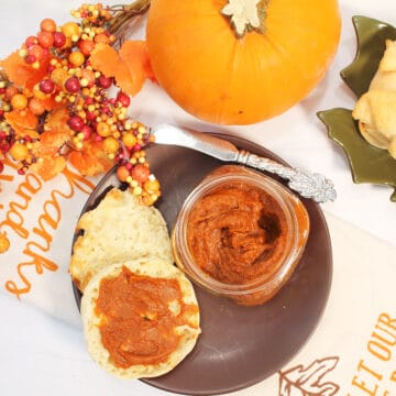 Overhead of butter spread on muffin with pumpkin and fall berries around it.