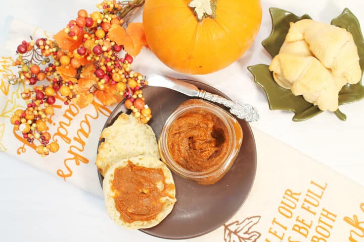 Overhead of pumpkin spread on muffin on brown plate with jar next to it.