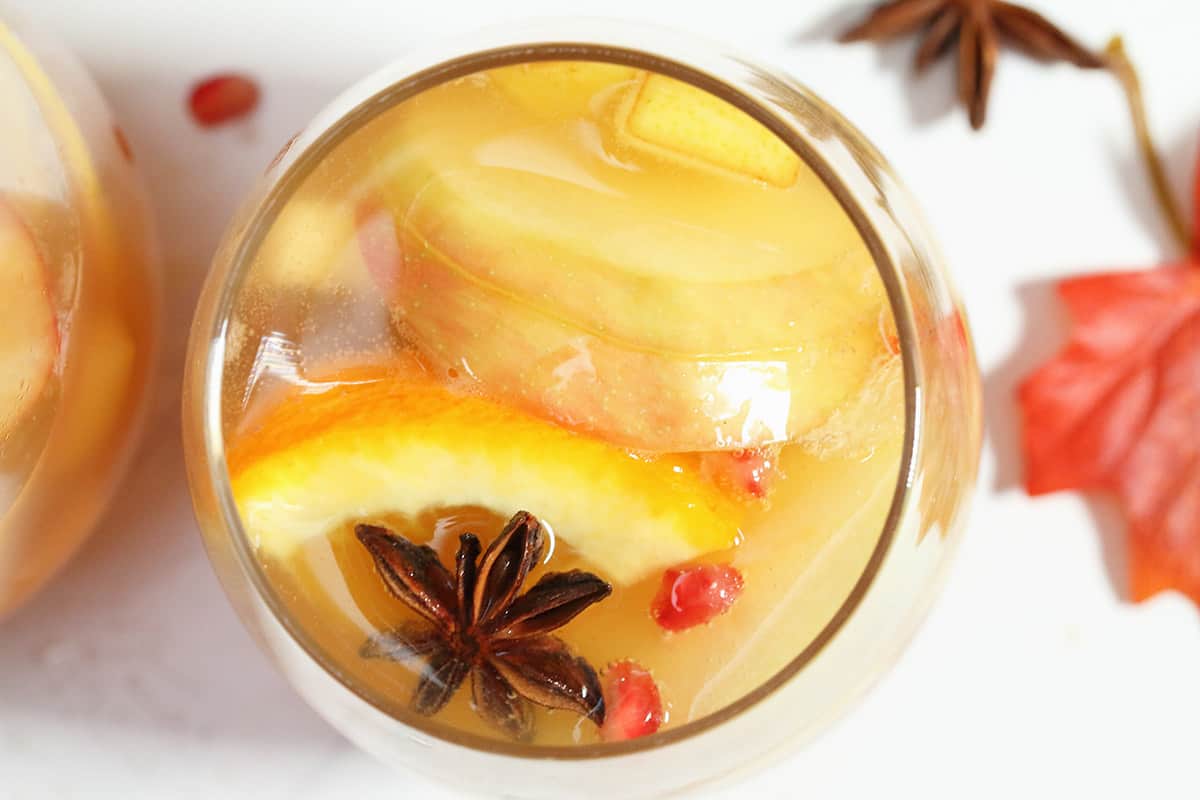 Overhead of glass of sangria on white table showing pieces of fruit and star anise.