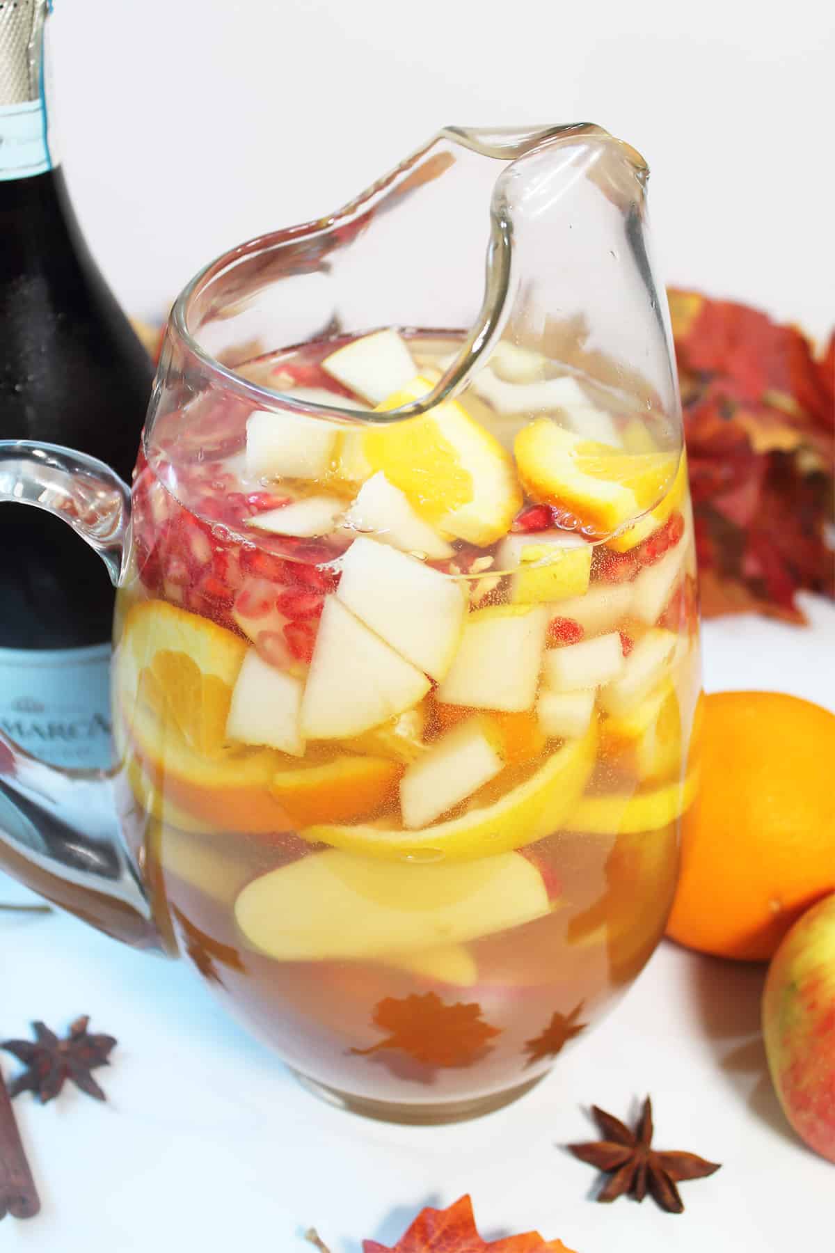 Filled pitcher on white table with star anise and champagne bottle.