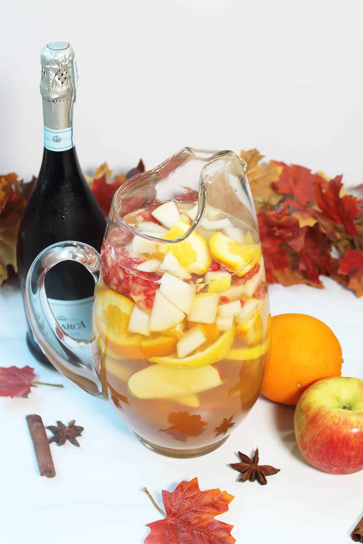 Fall sangria in pitcher with prosecco bottle and fall leaves.