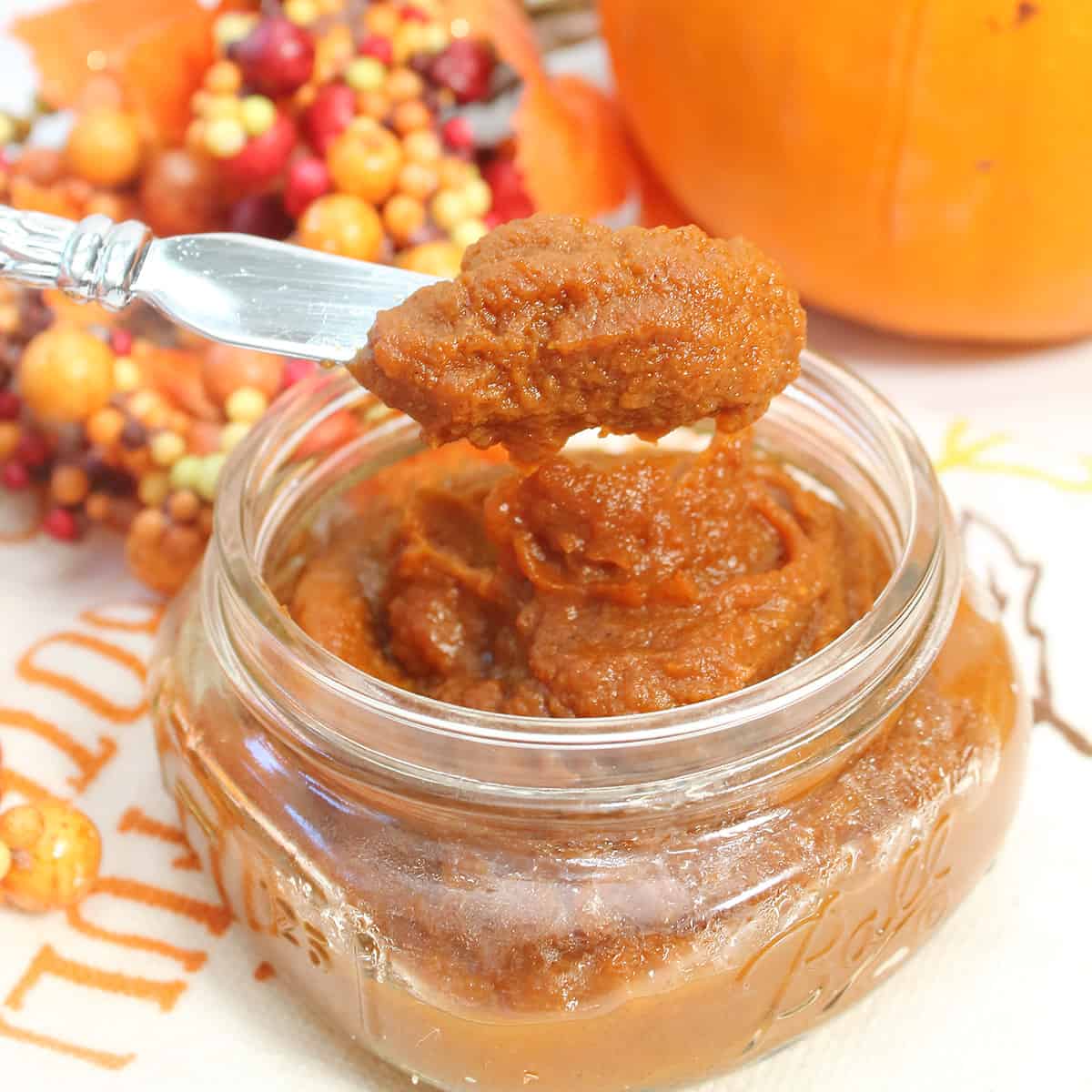 Scoop of pumpkin butter over jar with pumpkin in back.