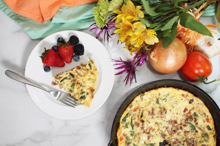 Overhead of serving on plate next to breakfast frittata in iron skillet. Vegetables and flowers around them.
