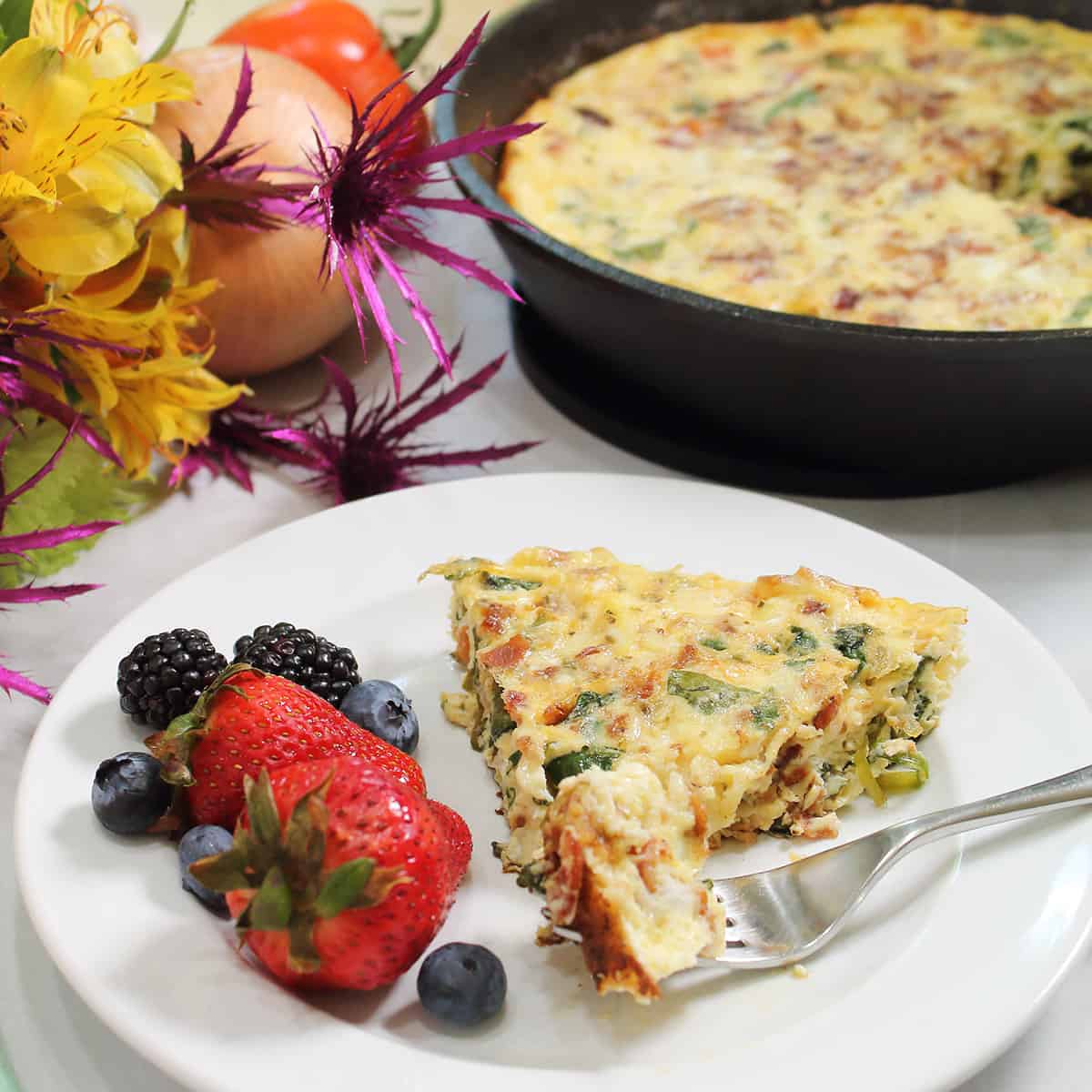Serving on white plate with bite on fork and fruit on the side and frittata in background..