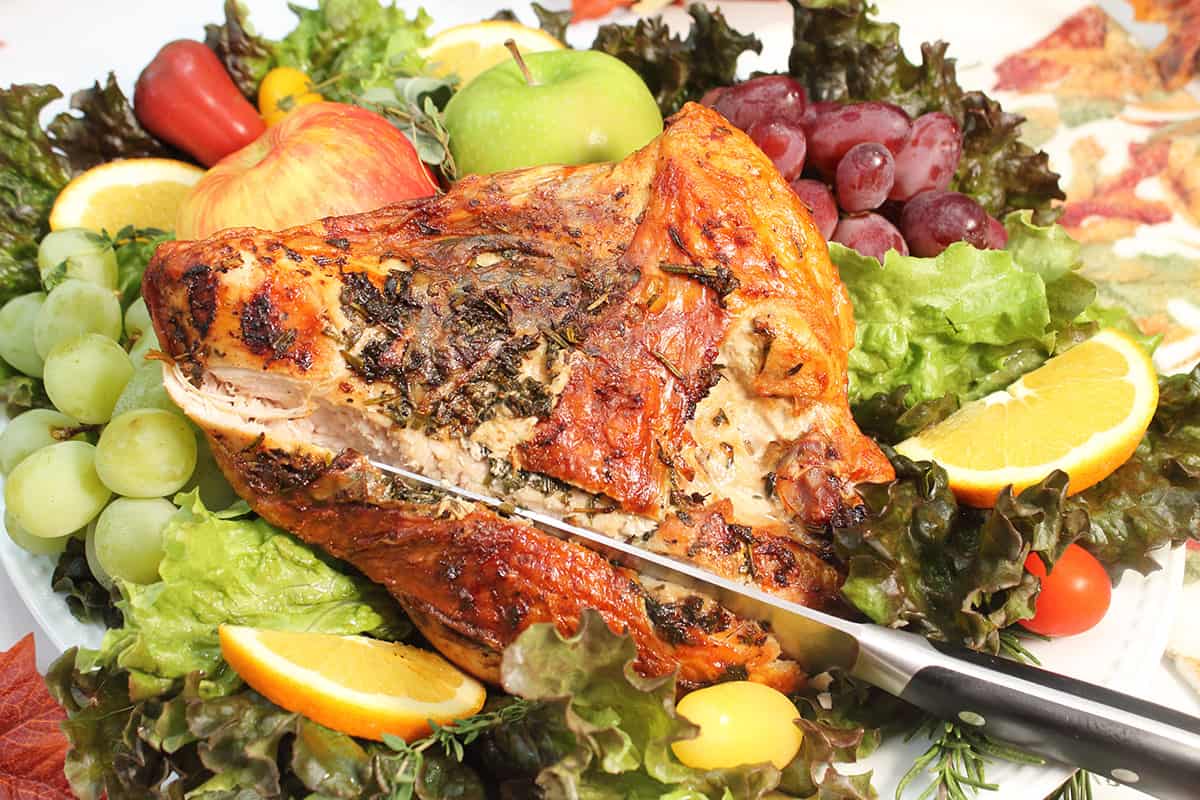 Closeup showing knife ready to carve turkey breast on platter with fruit.