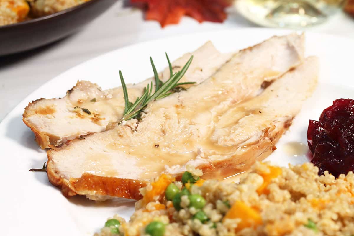 Sliced turkey with gravy on dinner plate with cranberry sauce and pilaf.