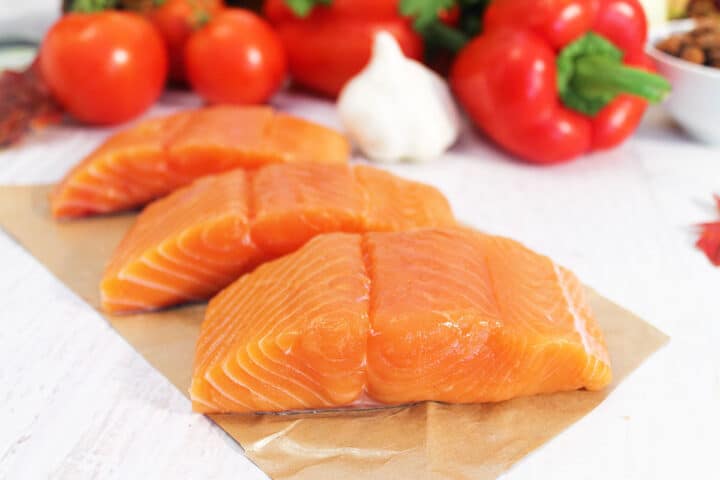 Raw salmon on brown parchment paper with vegetables in back.
