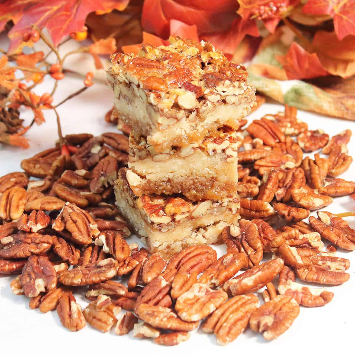 Stacked pecan pie bars with shortbread crust amidst pecans.