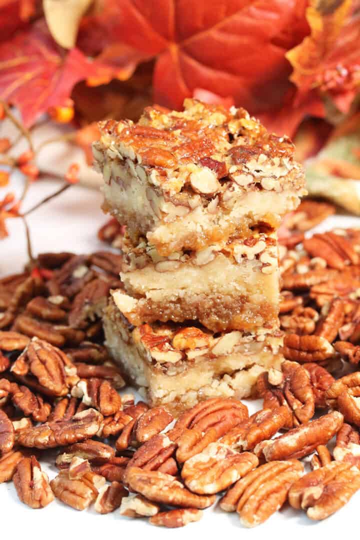 Stack of three pecan pie bars surrounded by pecans.