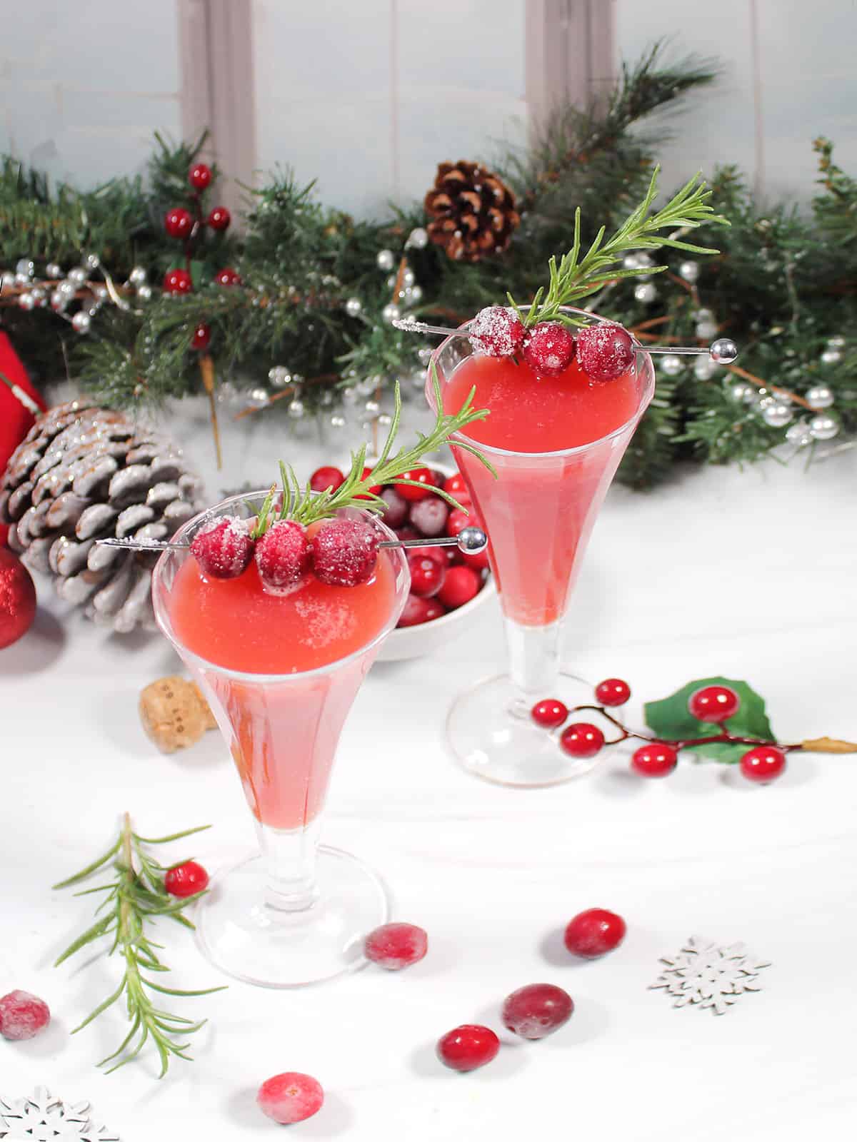 Two garnished Christmas cocktails by greenery.