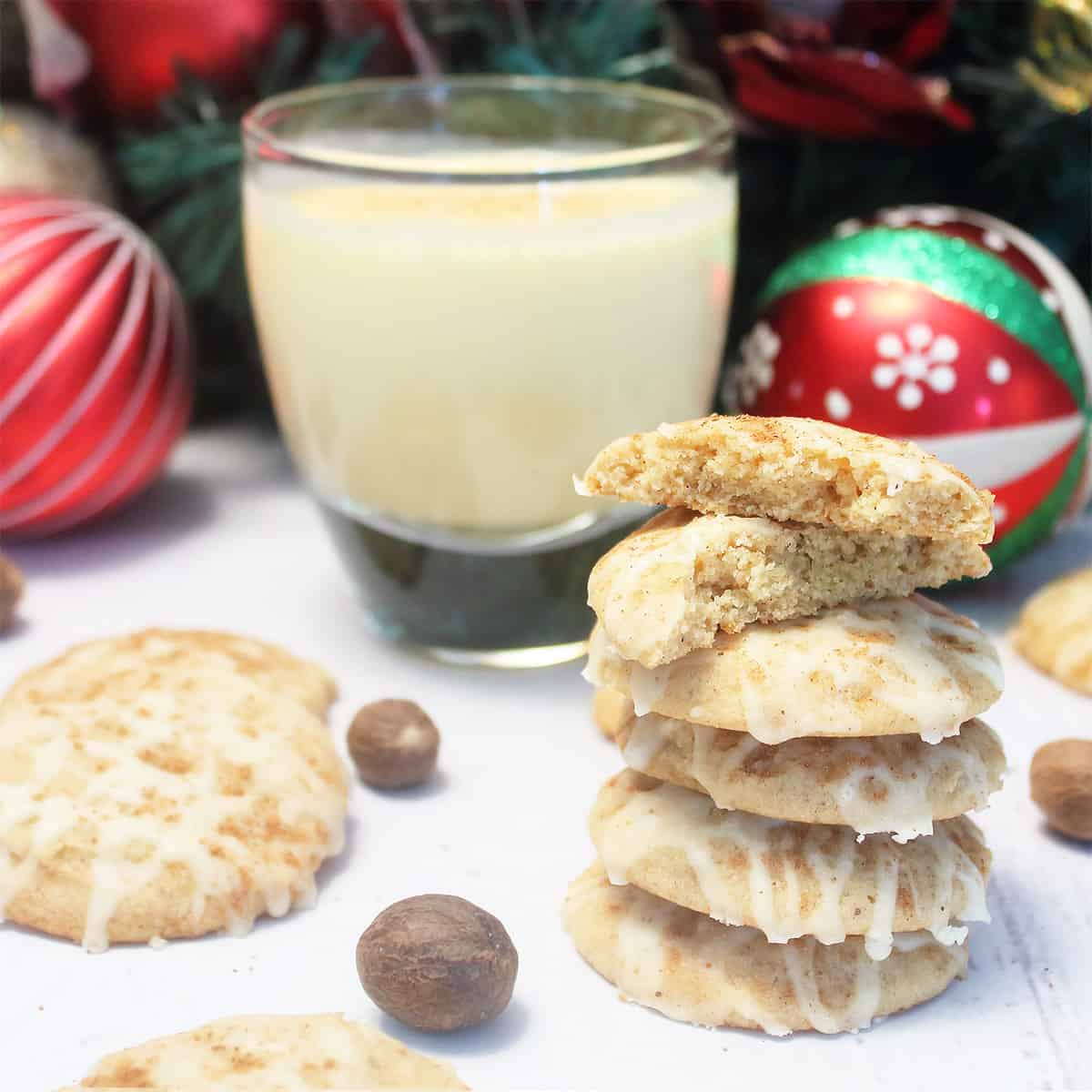 Eggnog Cookies with eggnog icing stacked in front of glass of eggnog.