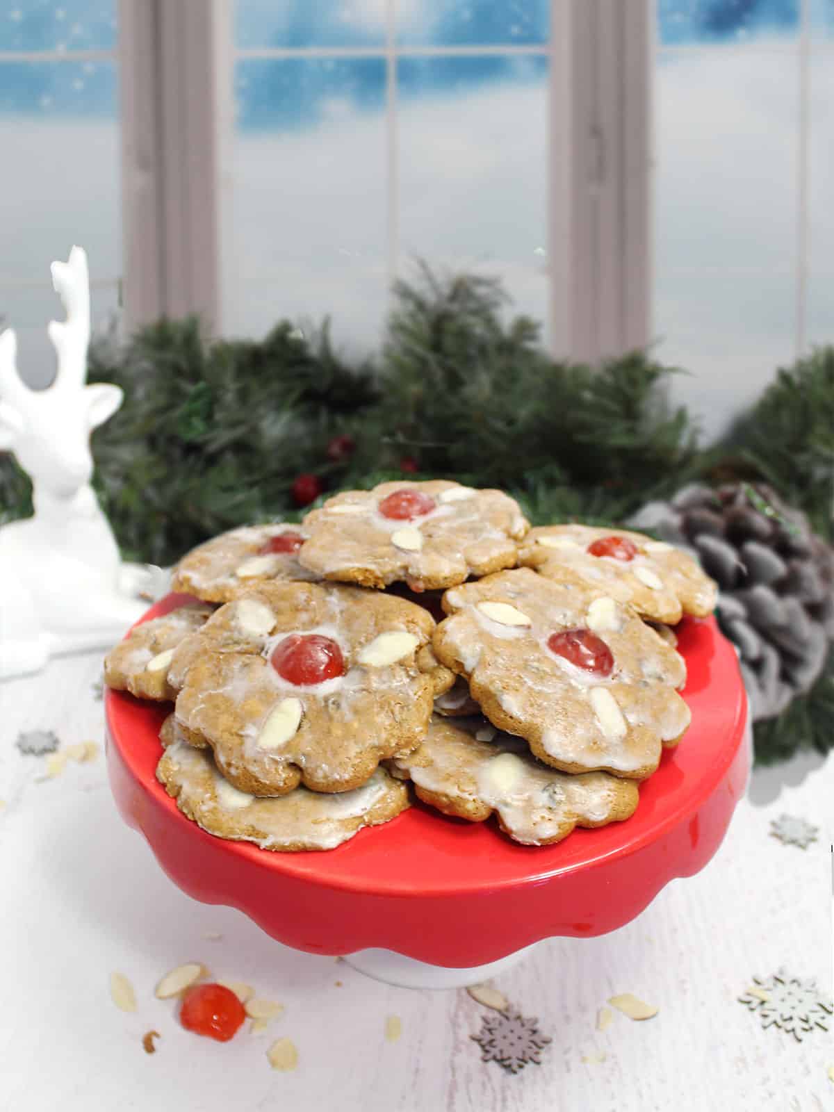Lebkuchens on red cake plate with greenery and reindeer in background.