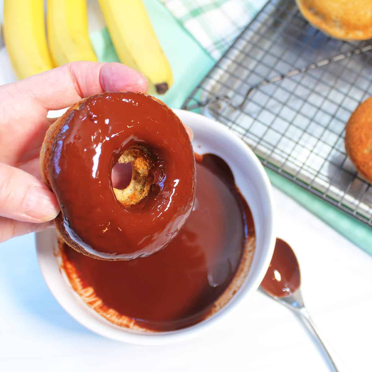 Dipping donut into the melted chocolate glaze.
