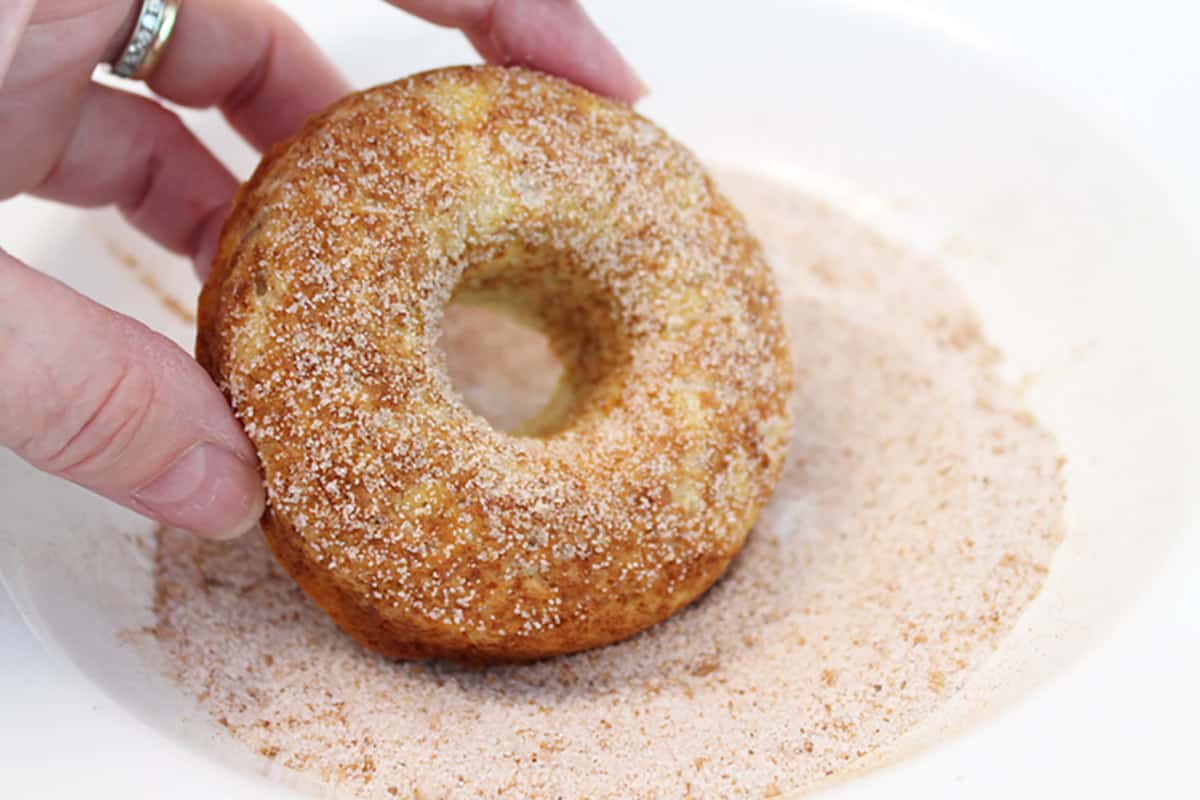 Dipping baked donut into cinnamon sugar.