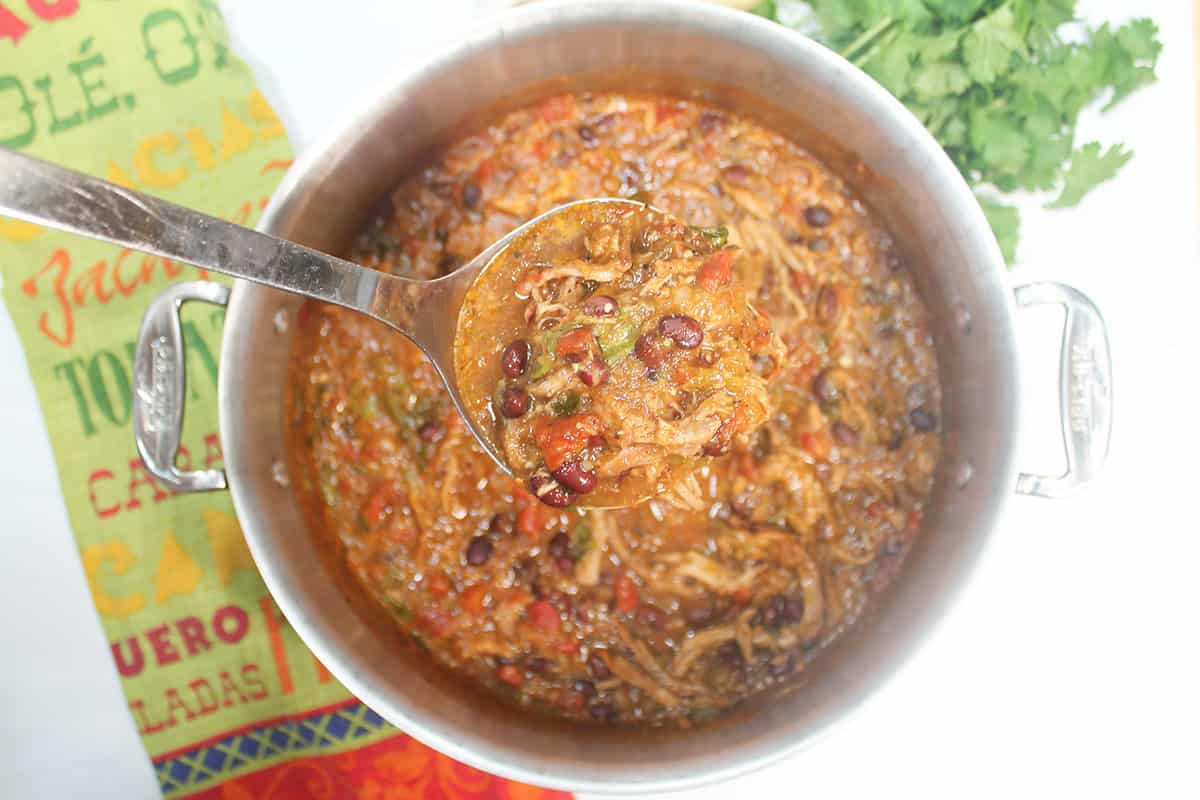 Ladleful of pork stew over stockpot.