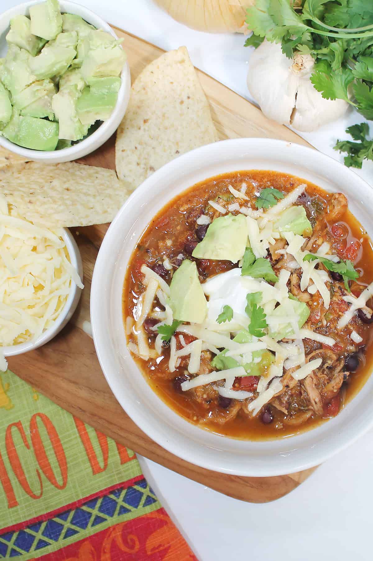 Overhead of garnished Mexican Pork Stew in white bowlwith sides of cheese and avocado.