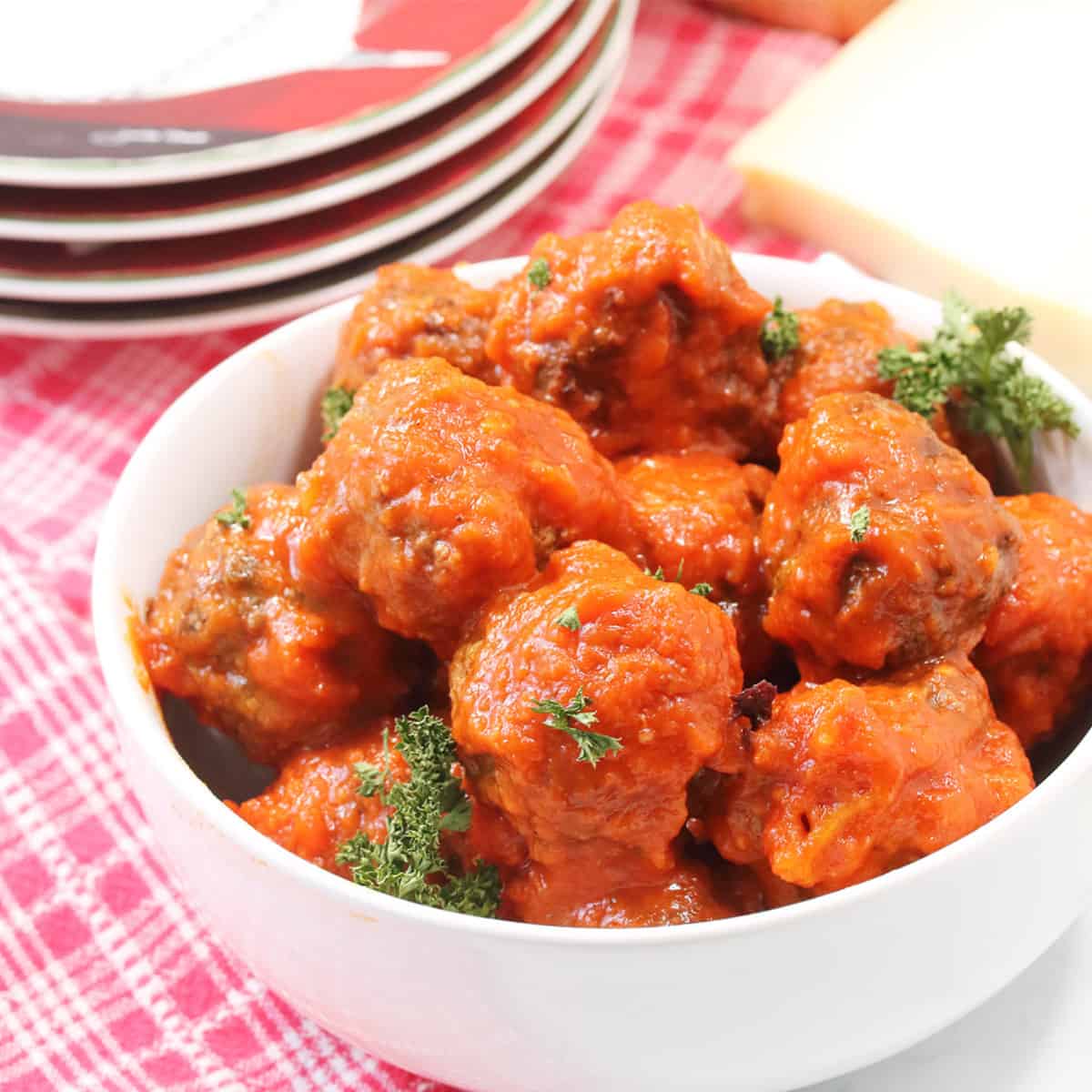 Meatballs in white bowl on top of red checkered towel.